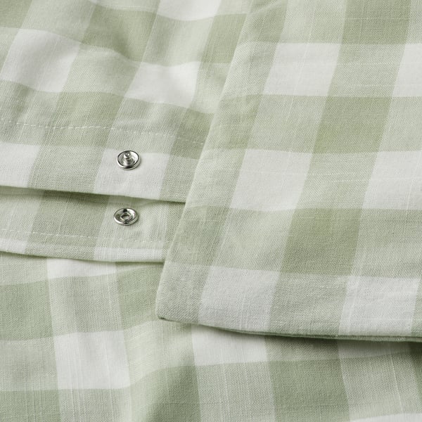 Close-up van groen-wit geruit dekbed, met metalen drukknoopsluitingsdetail.