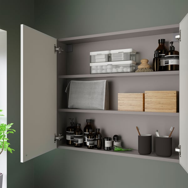 Open wandkast met planken voor toiletartikelen, dozen en een grijze doek in een badkamer. Toont nette organisatie binnenin.