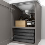 Open grijze badkamerkast, met grijze handdoeken eronder en toiletartikelen bovenop, met opbergfunctionaliteit.