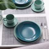 Tafelsetting met twee placemats, elk met een groene mok, schotel, diep bord en bestek.