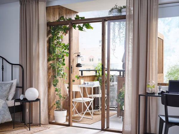 Lichte slaapkamer met balkon, bed, planten, eethoek buiten, grote ramen.