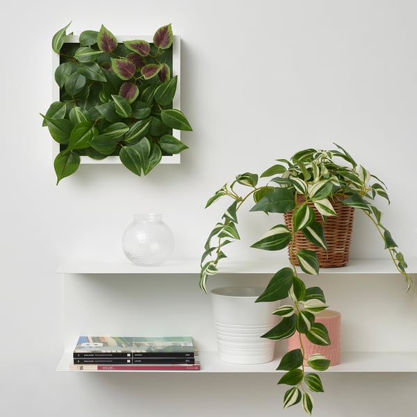 Witte wandplank met FEJKA kunst groene plant wandpaneel, mandplant, boeken en vazen. Paneelgrootte vergelijkbaar met boeken, aan de muur gemonteerd.