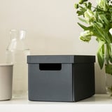 Op een tafel staat een grijze stoffen doos met een handvat. Het is ideaal voor het organiseren van kleine items zoals bureauaccessoires.