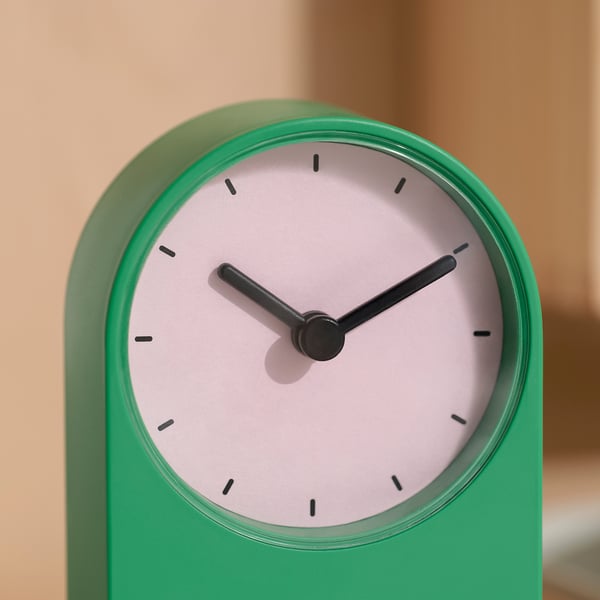 Eenvoudige groene klok met een gladde afwerking en slanke zwarte wijzers, tegen een neutrale achtergrond.