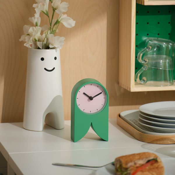 Groene FLODKRÄFTA-klok op wit aanrecht met vaas en sandwich.