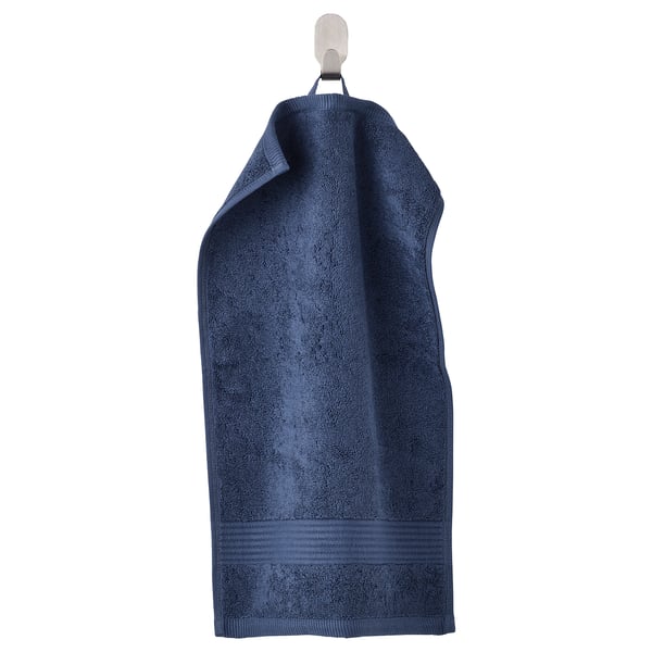 Aan een haak hangt een diepblauwe, dikke FREDRIKSJÖN handdoek netjes. Gemaakt van zacht, absorberend 100% katoen met een geweven rand.