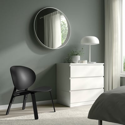 Minimalistische slaapkamer met stoel, dressoir, spiegel, paddestoellamp, lichtgroene muren.