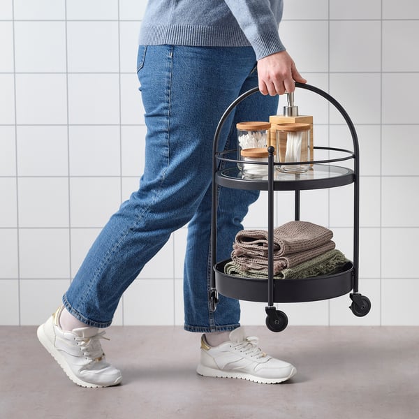 Persoon met FRÖSJÖN trolley van handdoeken en toiletartikelen, vergrendelbare wielen.