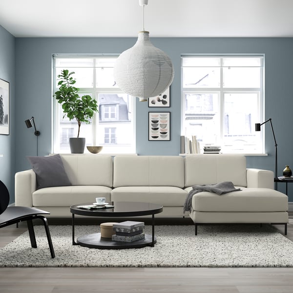 Moderne woonkamer met witte leren bank, lichtblauwe muren, deken, salontafel, lamp en hanglamp.