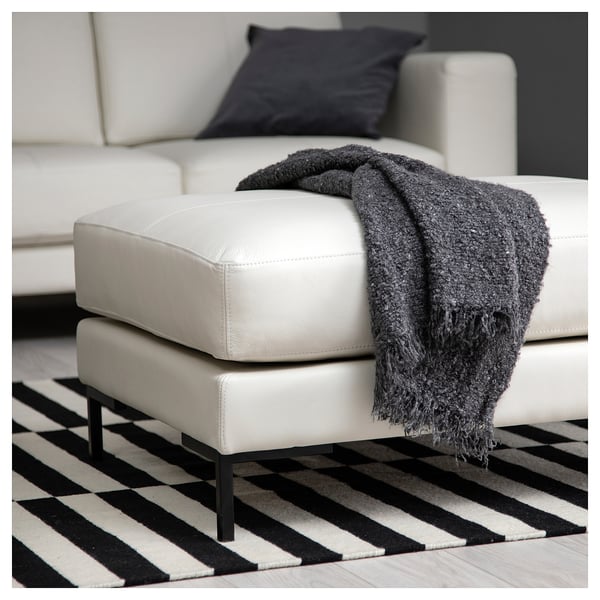 Moderne witte lederen poef met zwarte gefranjerde deken, op zwart-wit gestreept tapijt.