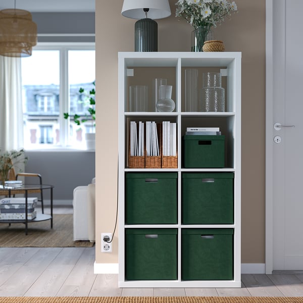 Witte kallax boekenkast met vier groene GJÄTTA stoffen dozen, decoratieve items bovenop.