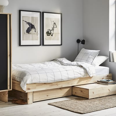 Minimalistische slaapkamer met GLAMBERGET lichthouten platformbed, wit rasterbeddengoed, abstracte kunst en zwarte wandlamp.