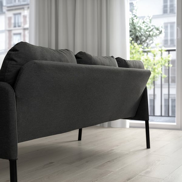 Moderne minimalistische leefruimte met houtskool GLOSTAD bank, strakke zwarte poten, pluche kussens, gepositioneerd bij groot raam, klein tegen muur.