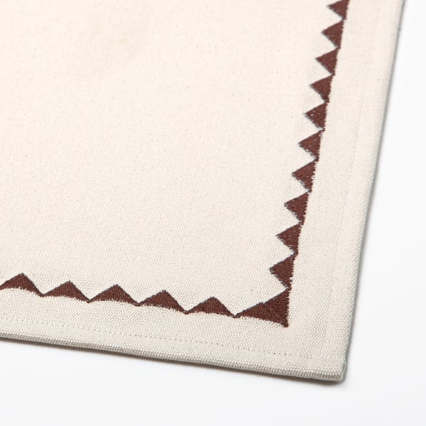 Vierkant beige textiel met bruine zigzagstiksels aan de randen.