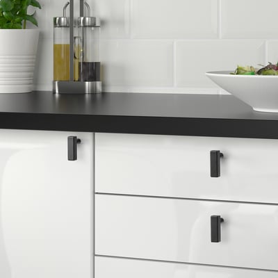 Moderne keuken met zwarte GRIBBOL knoppen, metalen ladegrepen, slakom, oliedispensers op donker aanrechtblad.