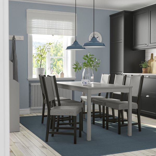 Moderne keuken met grijze HAUGA eethoek, stoelen met kussens, blauwe verlichting, raam, donkere kasten en vloerkleed.