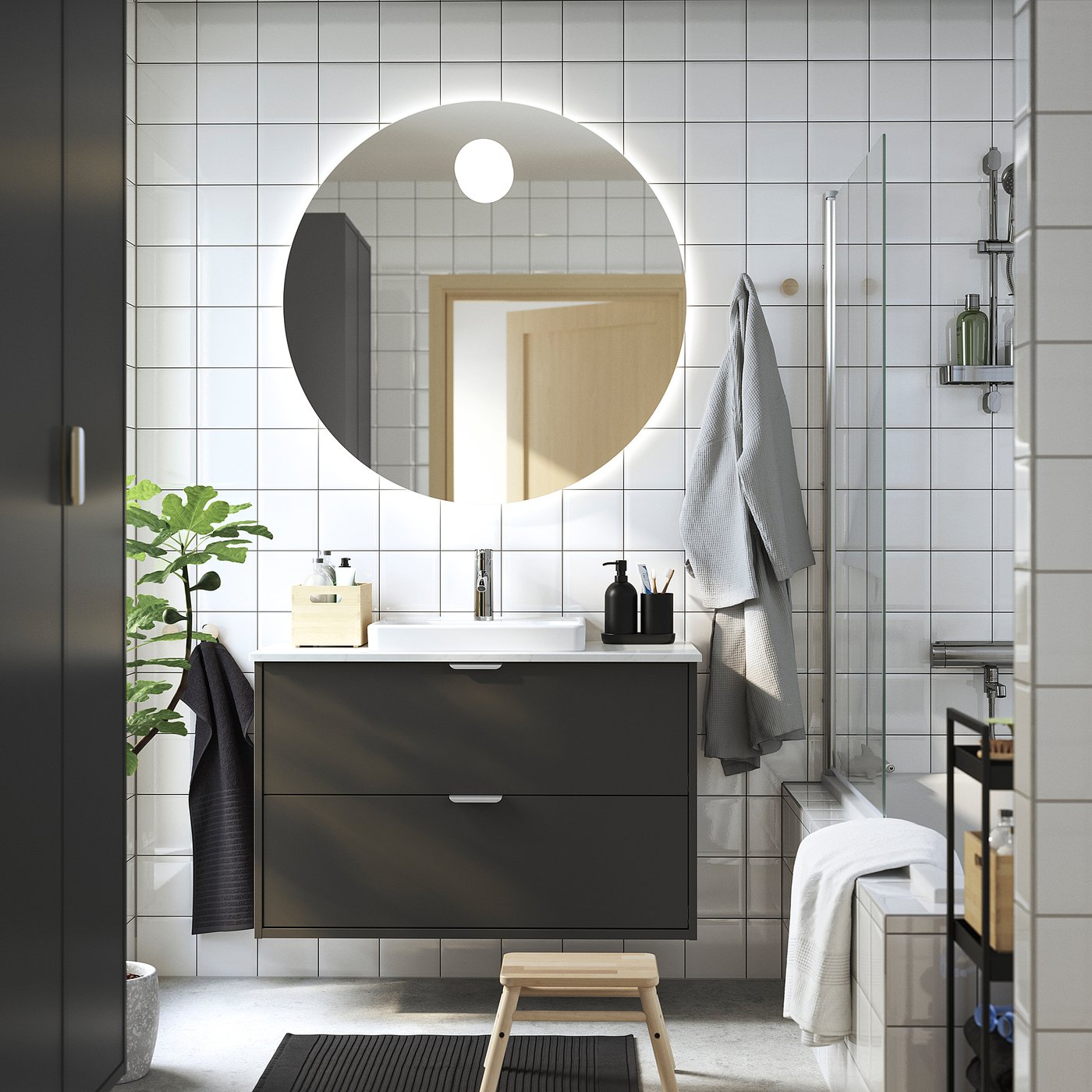 Moderne badkamer: HAVBÄCK zwart meubel, ronde spiegel, houten kruk, handdoeken, plant, glazen douche.