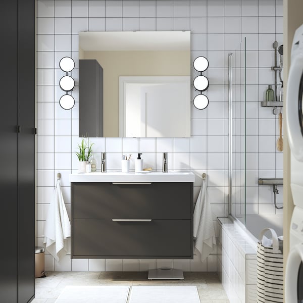 Moderne badkamer met zwart HAVBÄCK badmeubel, witte dubbele wastafel, grijze tegels en ronde spiegels. Witte handdoeken, zwarte wasdroger.