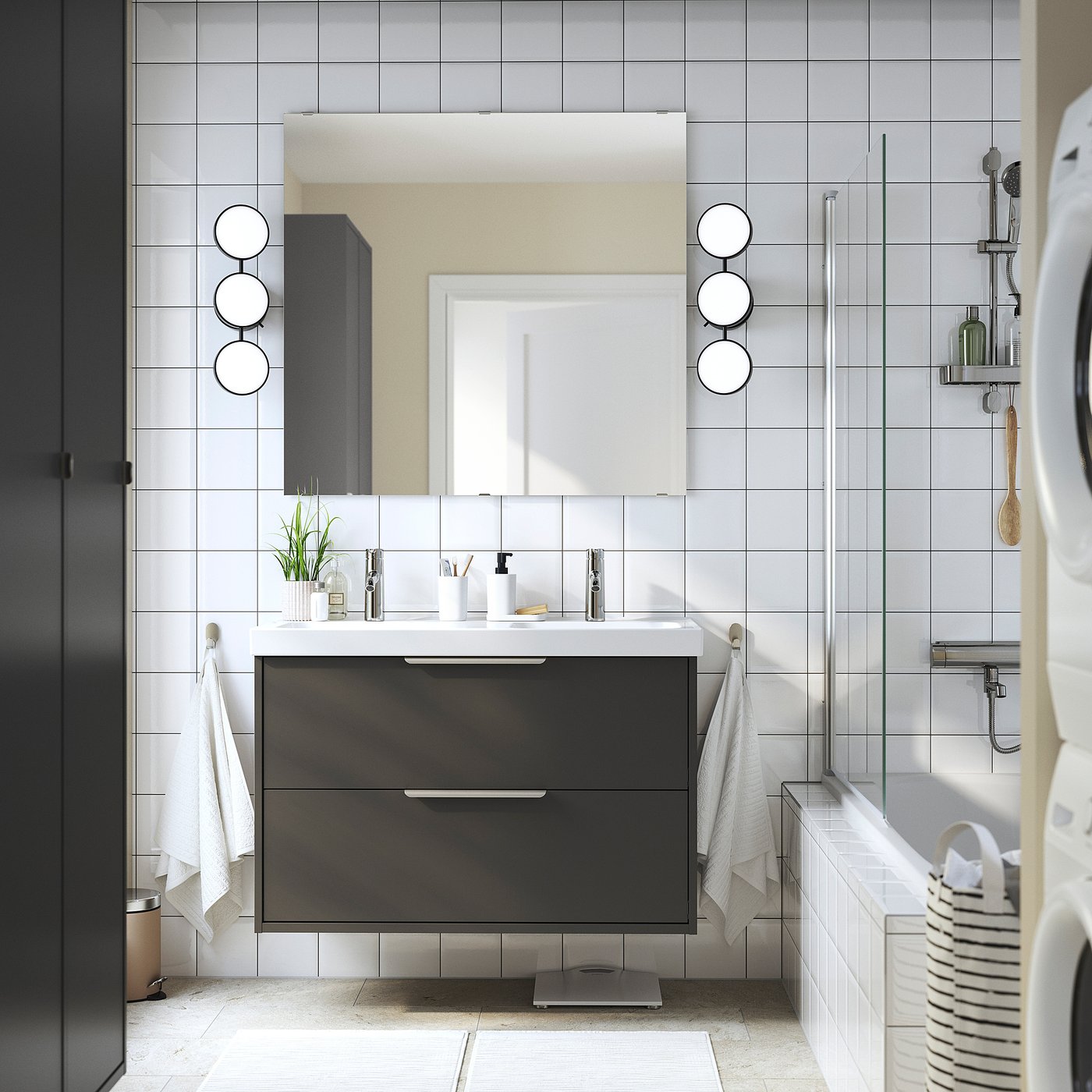 Moderne badkamer met zwart HAVBÄCK badmeubel, witte dubbele wastafel, grijze tegels en ronde spiegels. Witte handdoeken, zwarte wasdroger.