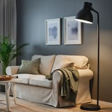 Stijlvolle woonkamer met zwarte lamp, witte bank, olijfkleurige dekens en groen.