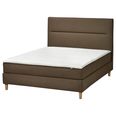 Een HEMFJÄLLET boxspring in bruin met een zacht hoofdeinde, houten poten en een witte matras.