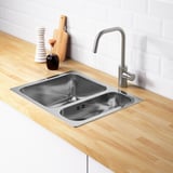 Roestvrijstalen spoelbak met twee spoelbakken, moderne kraan, houten aanrechtblad en netjes gerangschikte keukenaccessoires.