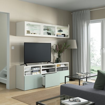 Moderne woonkamer met tv-meubel, bloemen, lamp en groot raam. De HJORTVIKEN opbergkasten bieden verborgen opbergruimte met stofbestendige deuren.