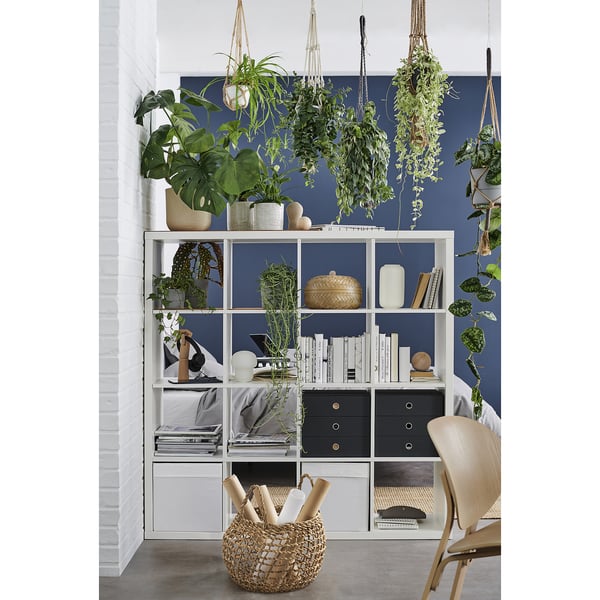 Modern kantoor aan huis met planken vol boeken, potplanten en een gevlochten mand. Donkerblauw en wit decor.