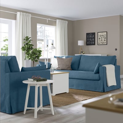 Blauwe woonkamer met HYLTARP bank, fauteuil, lamp en groot raam.