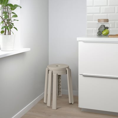 Moderne keuken met houten vloeren, witte kasten en gestapelde krukken. Een potplant en vruchten staan op het aanrecht.