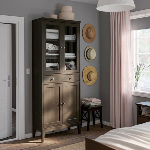 Modern grijs houten kabinet met glazen deuren, met handdoeken, in de buurt van raam met roze gordijnen.