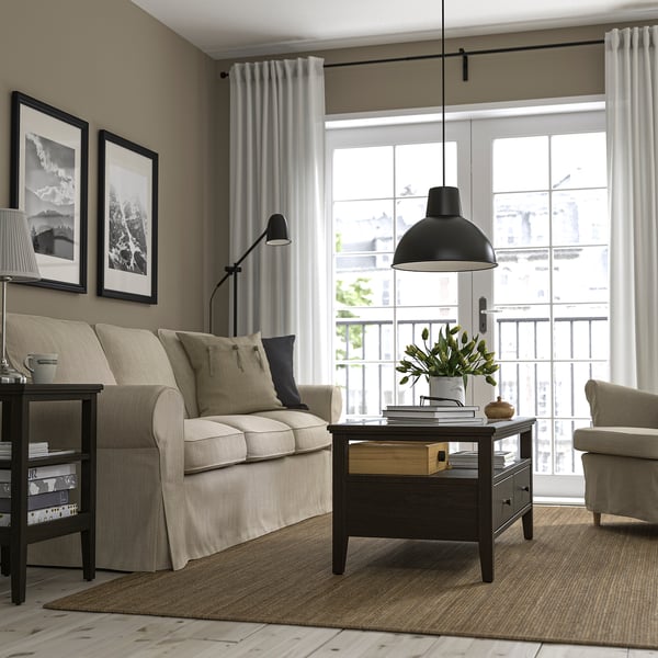 Moderne woonkamer met IDANÄS salontafel, beige meubels, zwarte hanglamp, grote ramen en wandfoto's.