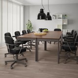 Modern kantoor met IDÅSEN-tafels en zwarte stoelen, hanglampen, groen en fruitschaal.