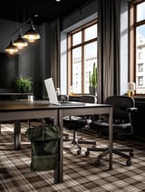 Moderne kantoorruimte met donkere meubels: IDÅSEN tafels, zwarte stoelen, groene rugzak, planten, hanglampen.