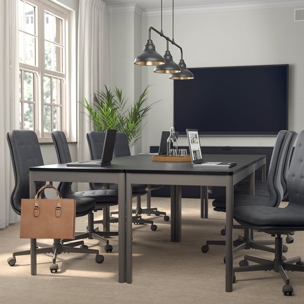 Moderne vergaderruimte met rechthoekige tafel, grijze stoelen, hanglampen, potplant en leren tas. Grote ramen.