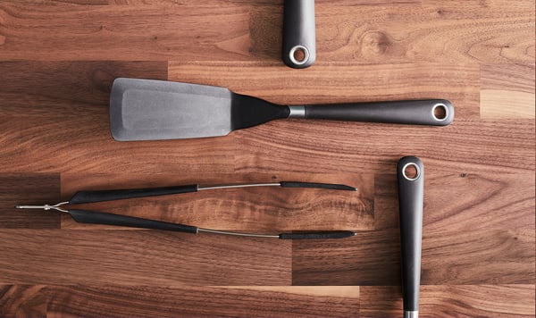 IKEA 365+ HJÄLTE zwart keukengerei: spatel, tang en twee draaiers met ergonomische siliconen handgrepen op een houten oppervlak.