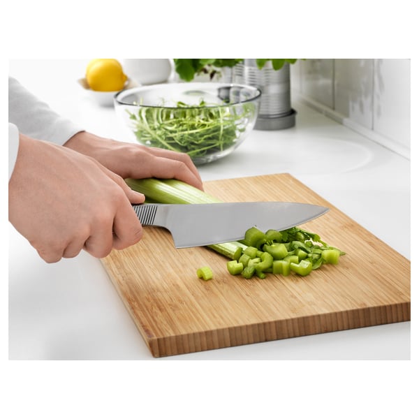 Hakken van bleekselderij op een houten snijplank met een roestvrijstalen koksmes.