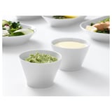 Twee kleine kommen bevatten groene dip en gele saus. Omgeven door salades, perfect voor het serveren van specerijen.