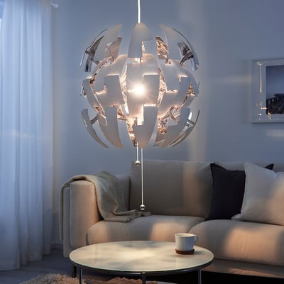 Witte ikea hanglamp over de bank in de woonkamer, die lichtpatronen werpt, met een mok op tafel.
