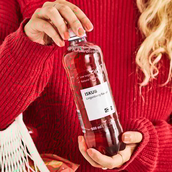 Persoon met een fles drank met rode bosbessensmaak van ISKUB, met een rode trui.
