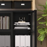 Zwarte IVAR opbergmeubel met gaasdeuren, met boeken, dossiers en decor op planken.