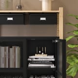 Zwart IVAR opbergmeubel met gaasdeuren en houten planken. Een deur open, met boeken en een decoratief item.