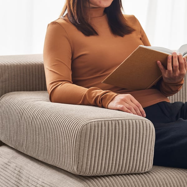 Een vrouw in een oranje shirt met lange mouwen leest een boek terwijl ze op een beige corduroy bank zit.