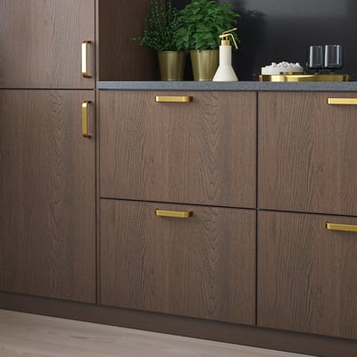 Donkerbruine houten keukenkasten met gouden handgrepen, strak en modern, met kleine groene potplanten en decoratieve voorwerpen op het aanrecht.