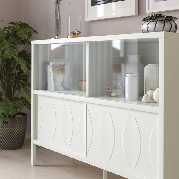 Witte kast met massieve en glazen deuren, met boeken en decor. Schuifdeuren besparen ruimte, ontwerp met reliëf, geïntegreerde verlichting beschikbaar.