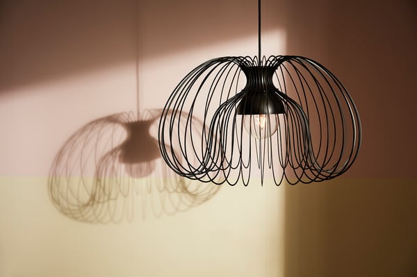 Twee moderne hanglampen met zwarte wireframe kappen werpen ingewikkelde schaduwen.