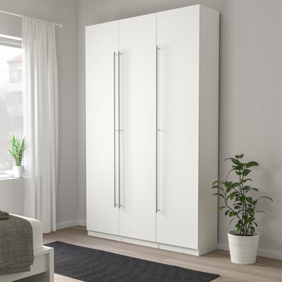 Moderne witte hoge kledingkast met strakke zilveren handgrepen, hoger dan plant en bed, minimalistisch design.