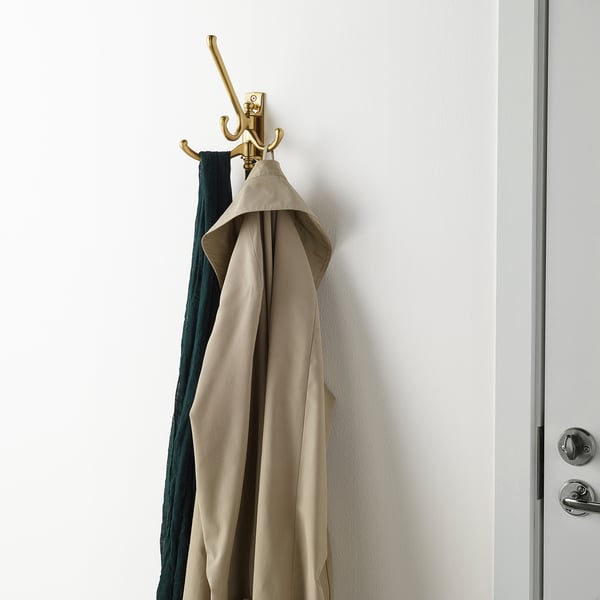 Gouden kapstok met beige jas op muur bij witte deur.