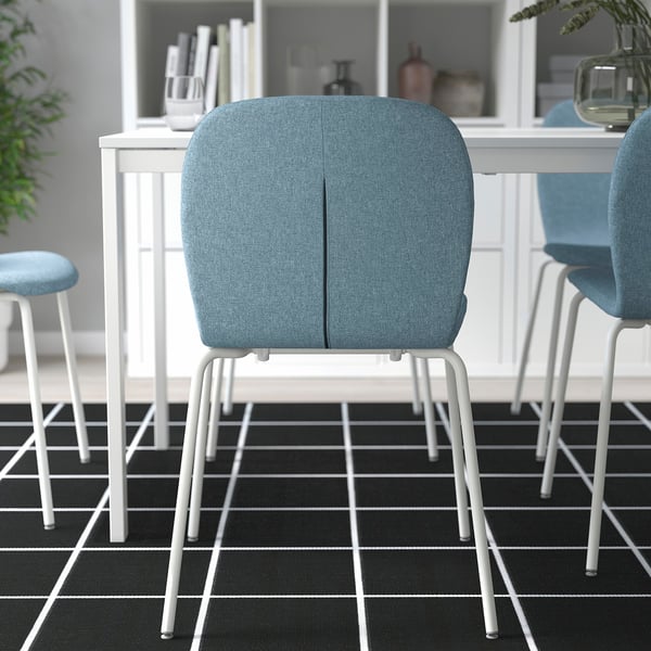 Drie moderne stoelen met blauwe kussens rond witte eettafel op zwart-wit geruite vloer.