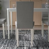 Moderne eetkamerstoel met grijs gestoffeerde rugleuning en zitting, hoge rugleuning voor comfort, geplaatst rond een tafel met gestreept vloerkleed.